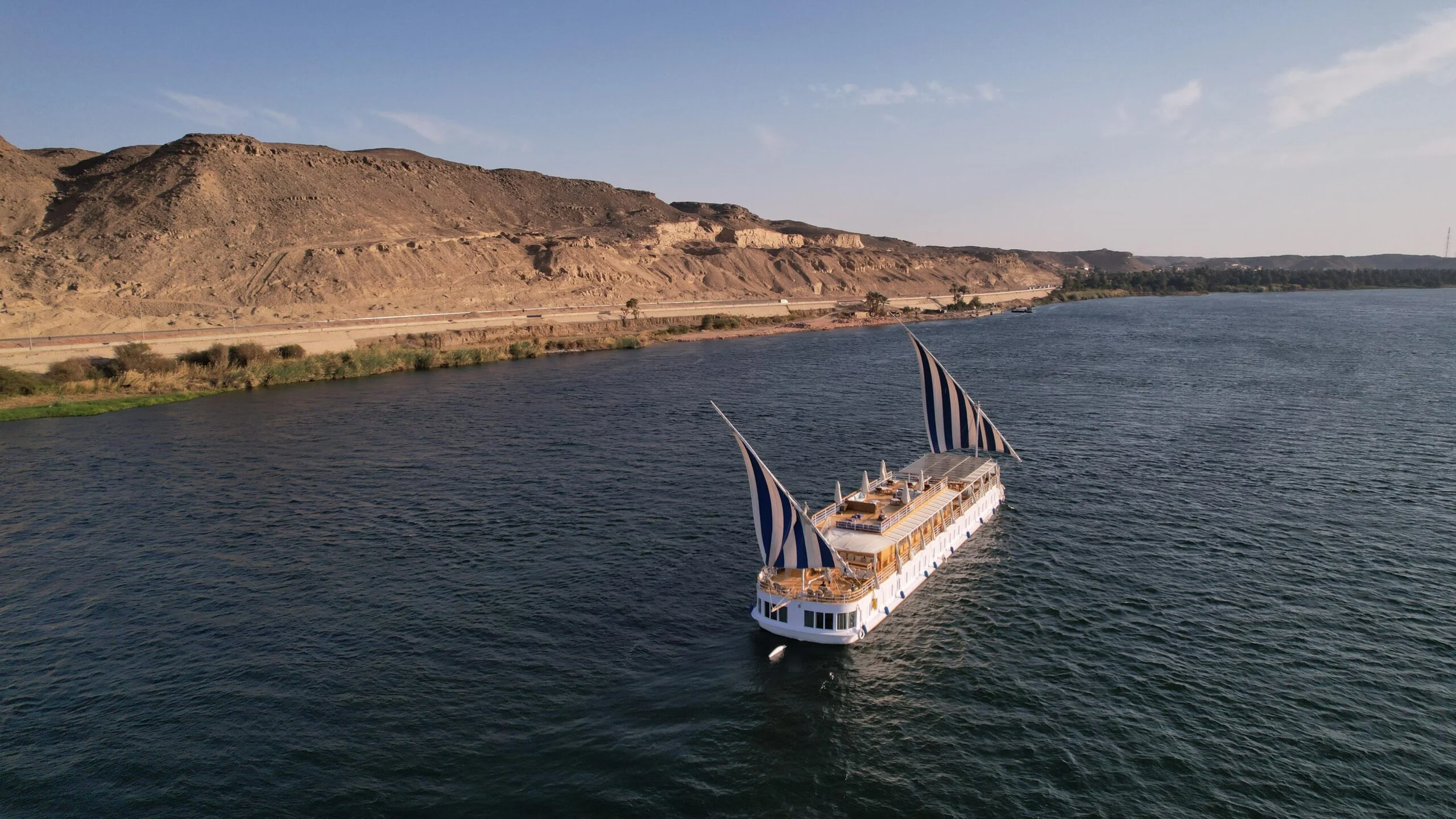 Stunning aerial drone view of Soul of the Nile Dahabiya sailing elegantly on the river with full striped sails deployed
